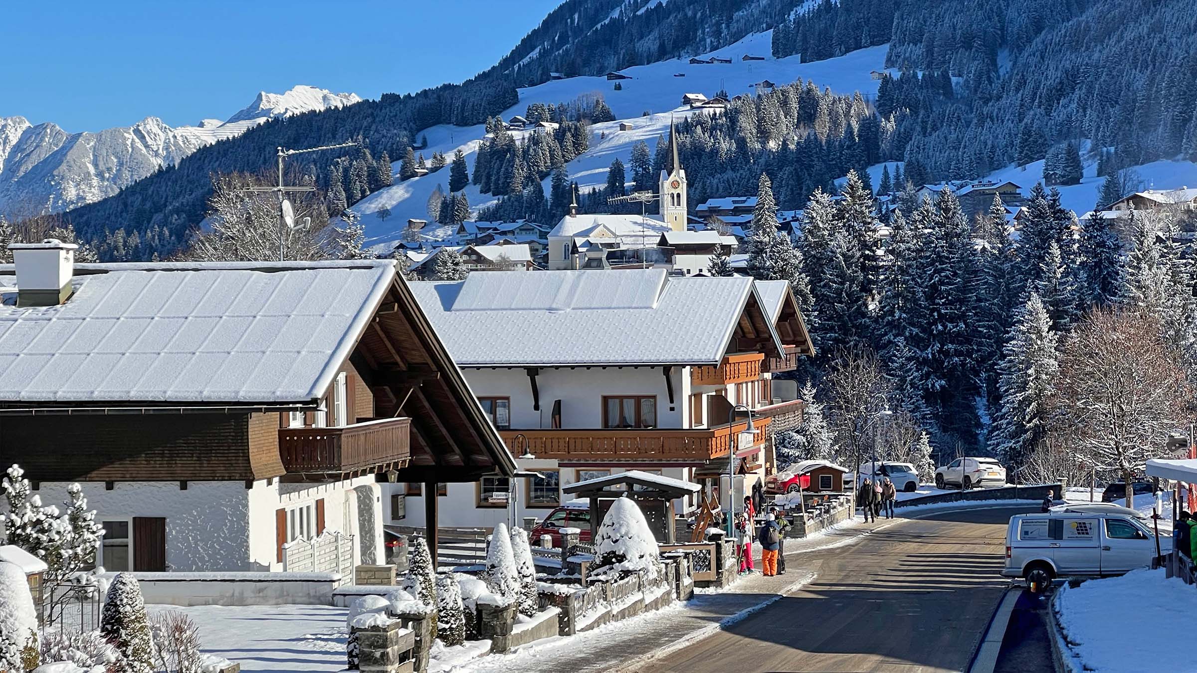 Verschneite Dächer, dahinter die Kirche von Riezlern und die bewaldeten Hänge