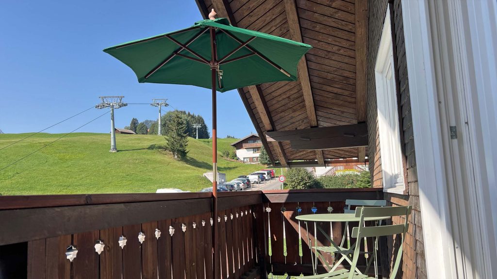 Balkon mit grünem Sonnenschirm, Blick auf die Wiese und die Bergbahn