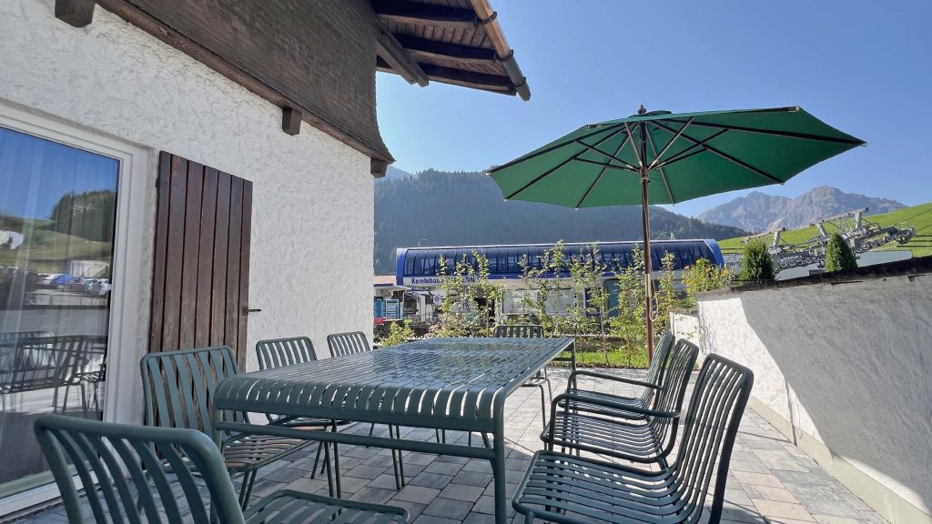 Terrasse mit Tisch, Stühlen und grünem Sonnenschirm